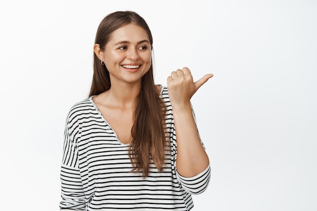 Image of candid happy woman pointing finger and looking right at advertisement, smiling and laughing over logo banner, white background