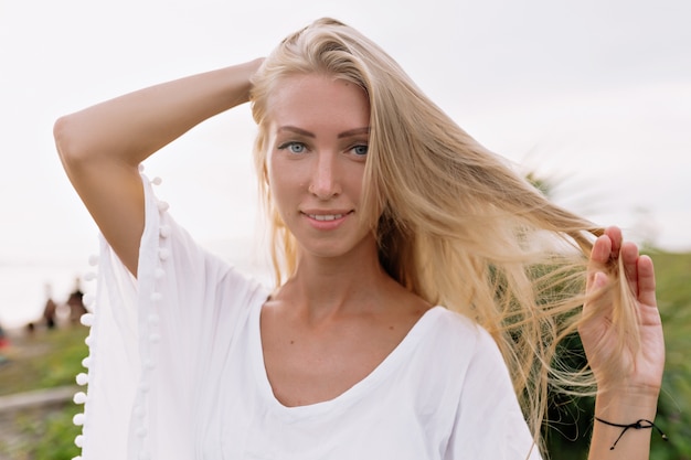 Foto gratuita immagine di una donna sorridente spensierata in una camicetta bianca che trascorre il tempo libero sulla spiaggia. atmosfera estiva. giorno soleggiato