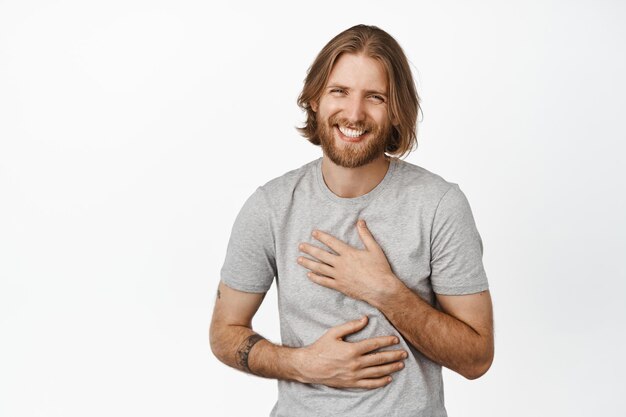 Image of caucasian handsome blond guy, bearded man laughing and smiling carefree, happy face of young male model in grey t-shirt, white background.