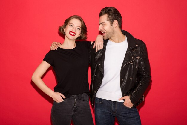 Image of cheerful punk couple hugging and posing together over red wall