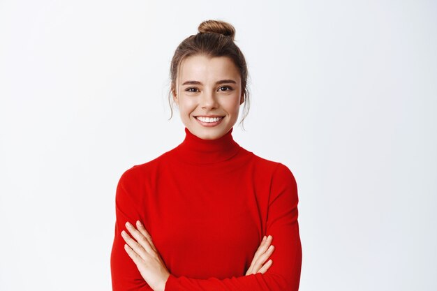 Image of confident blond woman CEO manager, cross arms on chest and look determined, smiling self-assured at front, white wall