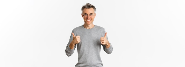 Foto gratuita immagine di un uomo di mezza età fiducioso e soddisfatto che sorride compiaciuto mostrando il pollice in su indossando felpa grigia