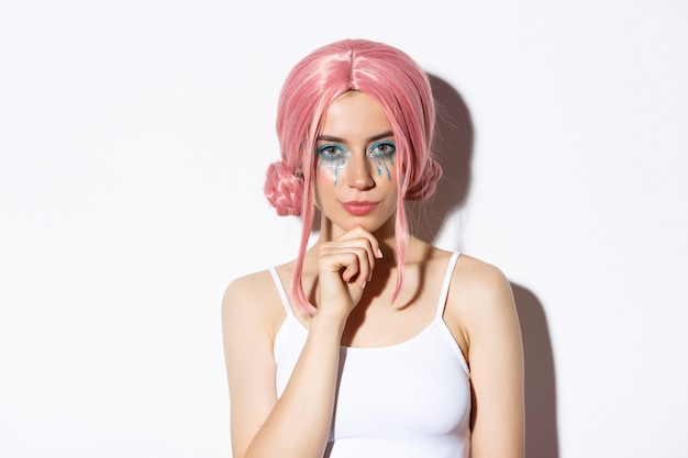 Image of confident woman in pink wig and halloween costume, thinking, looking at camera with interest, standing over white background