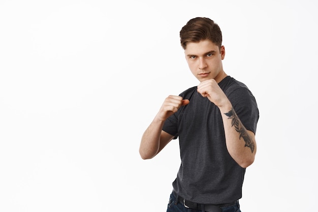 Free photo image of confident young man ready for fight, standing in boxing fighter pose, look determined, defending himself, standing over white background