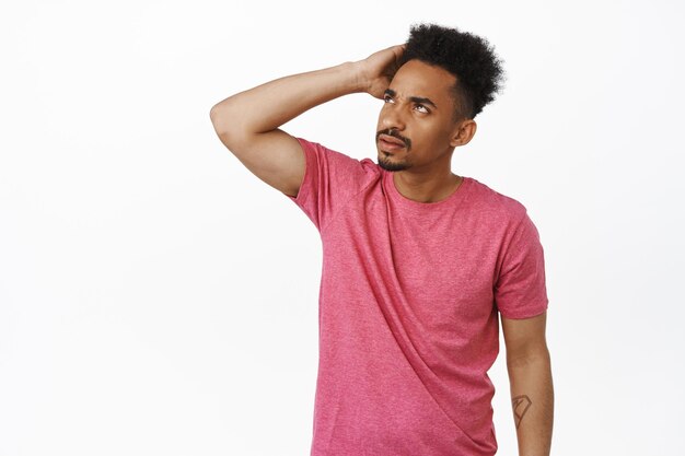 Image of confused african american man scratch head clueless, looking aside at upper left corner sale banner, frowning puzzled, cant understand smth strange, standing over white background