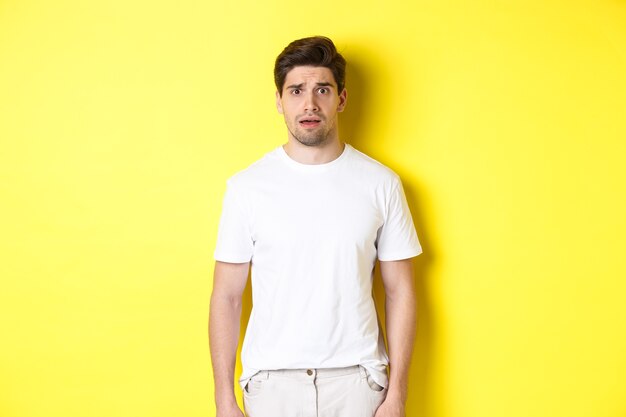 Image of confused and nervous man looking at something strange, frowning anxious, standing against yellow background.
