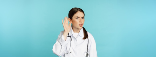 Free photo image of confused woman doctor cant hear you holding hand near ear and looking puzzled speak louder