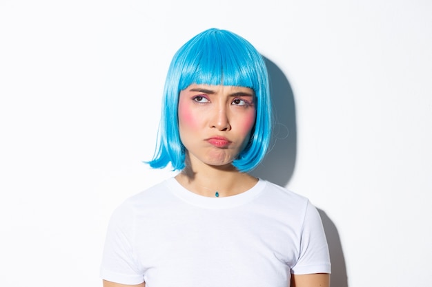 Image of cute asian girl in blue wig looking disappointed or jealous, sulking while stare at upper left corner