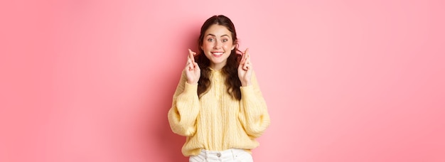 Free photo image of cute cheerful woman cross her fingers for good luck and looking hopeful at camera making wi