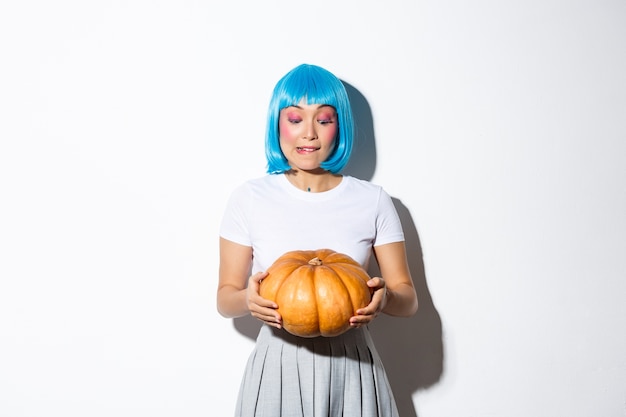 Image of cute girl picking pumpkin for halloween, wearing blue wig, standing.