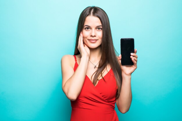 파란색 벽 위에 절연 귀여운 꽤 젊은 아가씨의 이미지. 휴대 전화의 디스플레이를 보여주는.