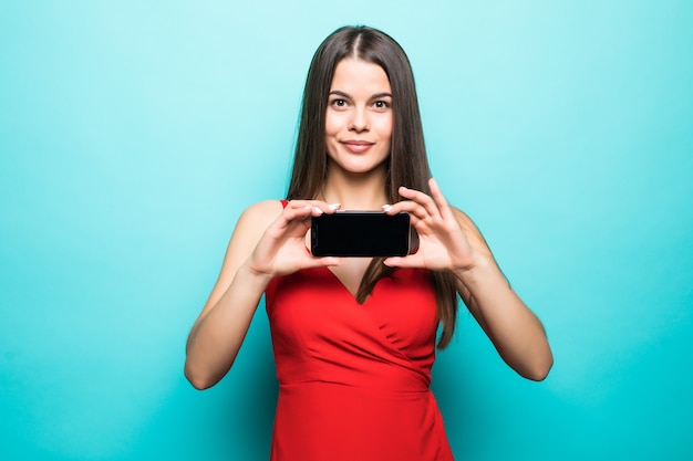 Immagine di carino piuttosto giovane donna isolata sul muro blu. mostrando il display del telefono cellulare.