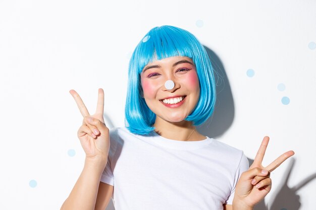 Image of cute and silly asian girl with confetti on her nose smiling happy and showing peace gesture