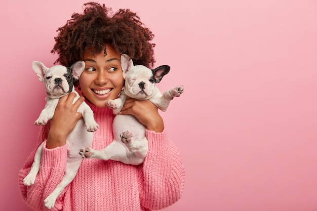 Free photo image of delighted female hostess poses with two cute puppies, looks happily away, takes picture with pets