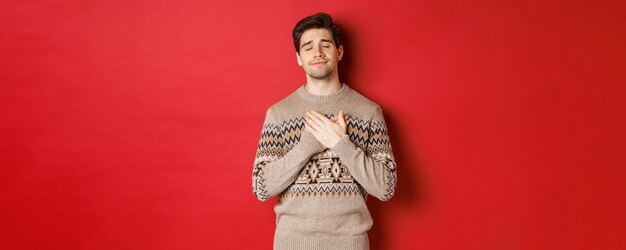 웃고 있는 마음에 손을 잡고 크리스마스 스웨터를 입은 꿈꾸고 행복한 매력적인 수염 난 남자의 이미지