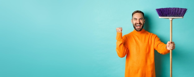 Image of encouraged and motivated man getting ready for cleaning holding broom and making fist pump