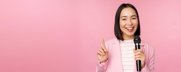 Immagine di una donna d'affari asiatica entusiasta che parla con il microfono che tiene il microfono in piedi