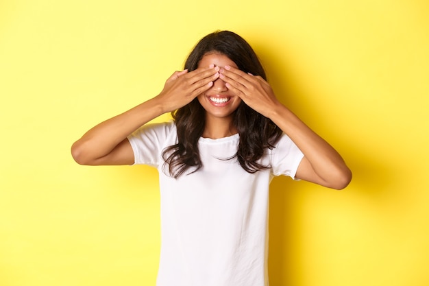 Image of excited africanamerican girl waiting for surprise smiling and covering eyes