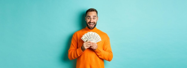 Free photo image of excited bearded guy holding money and rejoicing winning cash prize standing against light b