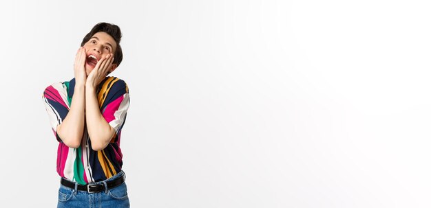 Image of excited gay man shouting of joy and looking up feeling ecstatic standing against white background