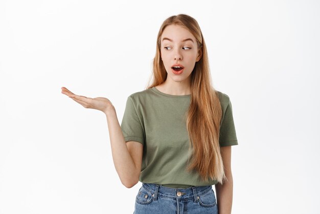 Image of excited girl looks at her hand holding copyspace with interest display item on open palm standing against white background Advertisement concept