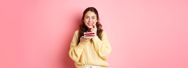Image of excited girl thinking of eating delicious cake biting finger from temptation and looking th