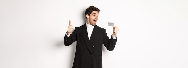 Free photo image of excited handsome businessman showing credit card and thumbup standing against white backgro