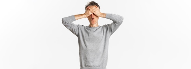 Free photo image of excited middleaged guy in grey sweater cover eyes with hands and looking amazed while waiti