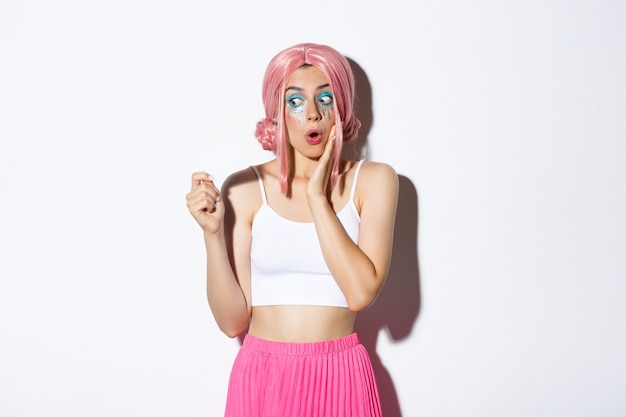 Free photo image of excited silly girl in pink anime wig and bright makeup, looking amazed at credit card, shopping for holidays, standing.