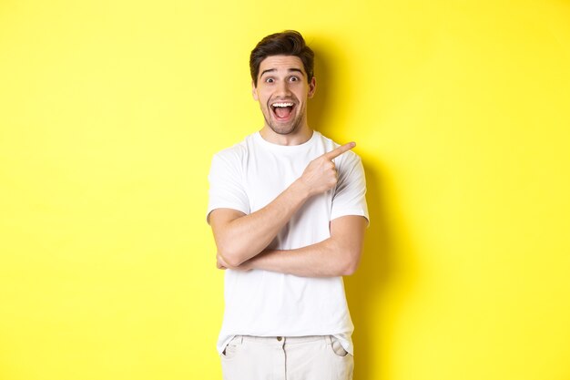 Image of excited smiling man showing black friday offers, pointing finger right and looking amazed, standing over yellow background.