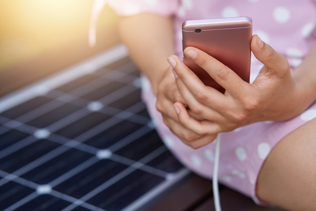 Immagine di una donna senza volto in abito rosa che carica il suo smartphone sul caricabatterie multiuso solare gratuito, energia gratuita per tutti