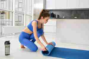 Free photo image of fitness girl preparing her living room for workout training unwrapping yoga mat for