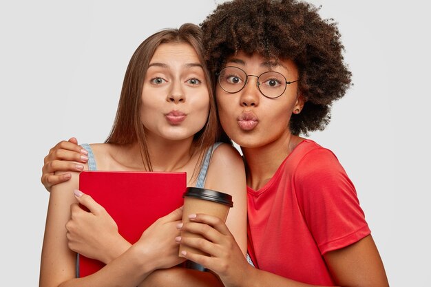 Image of friendly interracial young women embrace each other affectionately, give kiss