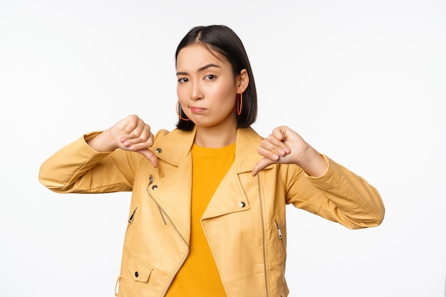 Free photo image of fully disappointed asian woman showing thumbs down shaking head displeased dislike smth standing over white background