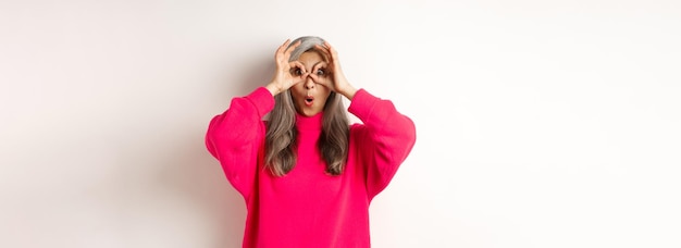 Free photo image of funny asian grandmother looking through hand glasses with surprised and amazed face checkin