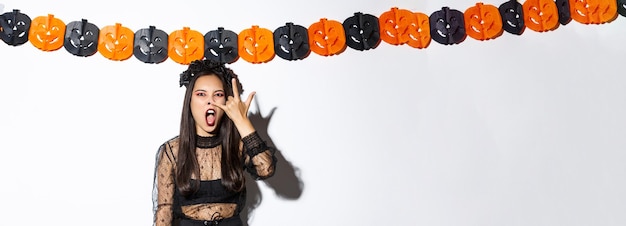 Free photo image of funny asian woman in witch costume grimacing wearing gothic lace dress and standing against