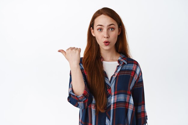 Image of girl look surprised, say wow and pointing left at interesting logo. Curious woman asking question about promo offer, showing advertisement, white background