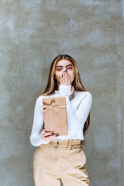 Image of a girl model holding a paper present over stone 