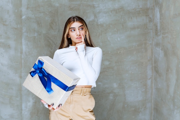 Free photo image of a girl model holding a present box with bow isolated over stone