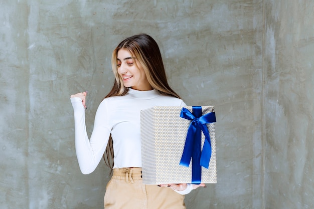 Image of a girl model holding a present box with bow isolated over stone