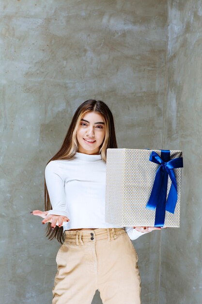 Image of a girl model holding a present box with bow isolated over stone