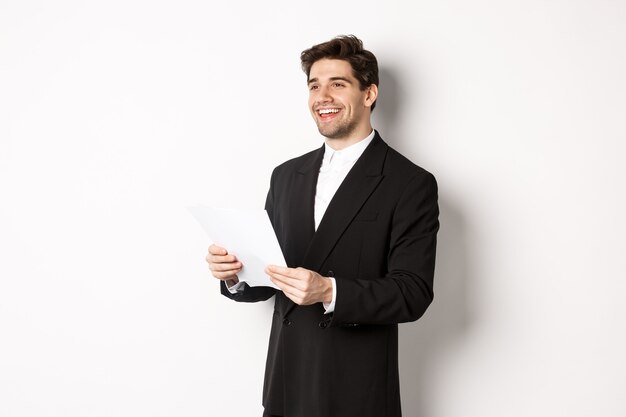 Image of handsome businessman in suit, holding documents and smiling, standing against white background