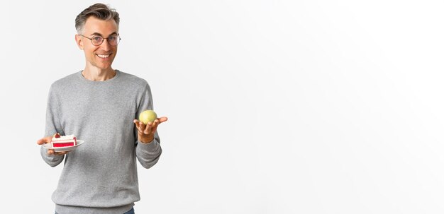 Image of handsome and healthy middleaged man in glasses recommending eat apple instead of cake stand