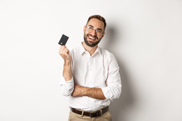 Image of handsome man thinking about shopping and holding credit card, looking at upper left corner thoughtful