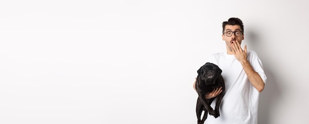 Free photo image of handsome young man holding cute dog and gasping surprised pet owner staring at camera shock