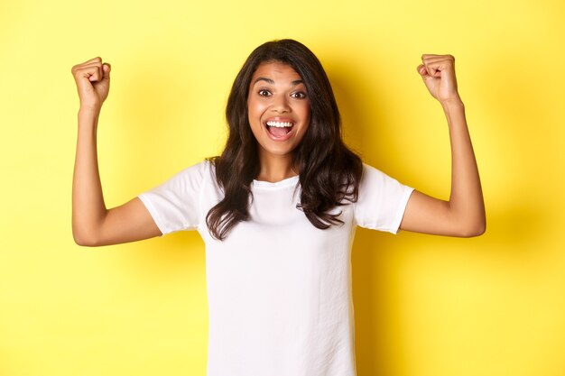 Image of happy africanamerican girl achieve goal and celebrating victory raising hands up