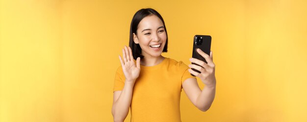 Image of happy beautiful asian girl video chatting talking on smartphone application standing agains