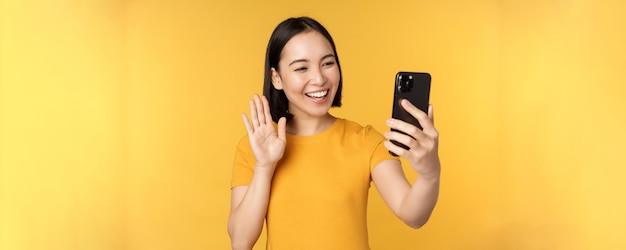 Image of happy beautiful asian girl video chatting talking on smartphone application standing agains