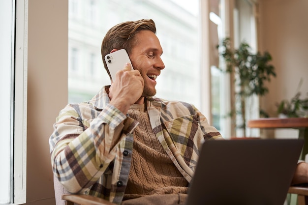 Image of happy cafe visitor man with laptop calling a friend over the phone businessman talking on