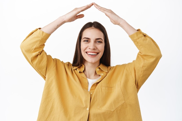 Image of happy candid woman laughing smiling and showing secure rooftop making roof with hands above head being protected standing over white background